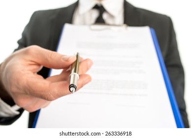 Businessman or salesman handing over a contract attached to a clipboard for signature offering a ballpoint pen in his hand with focus to the pen.