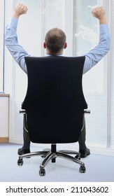 Businessman Sat In Office Chair With Armes Raised In Success