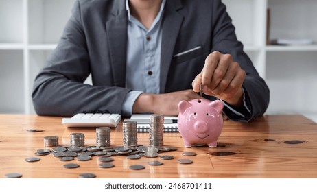 Businessman saving money with piggy bank and coins on desk, financial planning and investment concept.