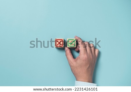 Businessman select green correct sign mark between Red Cross mark which print screen on wooden cube block for approve and reject business project proposal concept.
