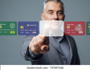 Businessman selecting a credit card on a visual interactive interface and choosing a payment method, he is touching a blank card; online banking and payments concept