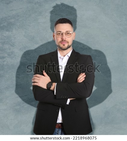 Businessman and shadow of strong muscular man behind him on grey wall. Concept of inner strength
