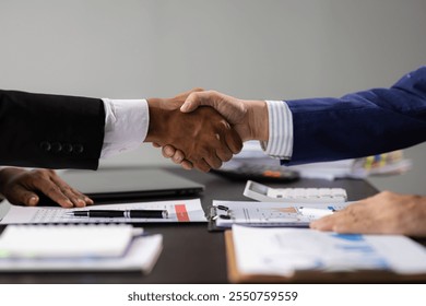 Businessman shaking hands over a desk with charts and graphs, successful business deal. - Powered by Shutterstock