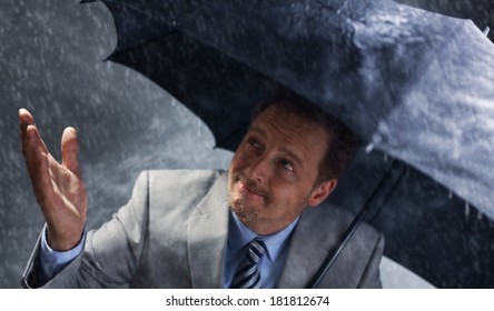 Businessman Sheltering From The Rain Under An Umbrella Looking Up At The Change In The Weather As The Sun Starts To Come Out