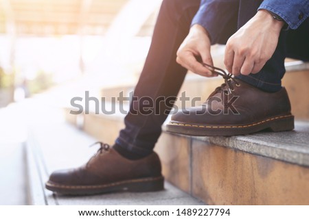 Businessman in a shirt jeans tie up shoelace on wearing brown leather shoes sitting staircase background. Men's style.  Leave space for writing descriptive text