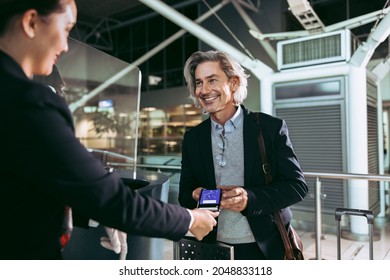 Businessman showing electronic boarding pass to flight attendant at airport check in counter. Smiling male traveler doing digital check in at airport terminal.