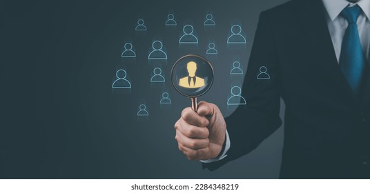 Businessman showing human resources virtual icon or HRM, magnifying glass focus on manager icon, one of employee icons for leadership service, leading organization in recruiting and prospecting.