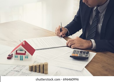 Businessman signing contract agreement with document, money and house model on the table - real estate, properties and investment concepts