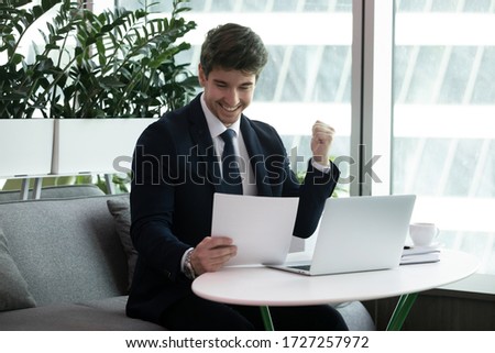 Businessman sit at desk read paper financial documents feels excited by sales increase, celebrate profitable deal, receive lucrative contract, good project results, entrepreneur get bank loan approval