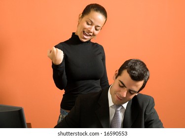 Businessman Sits At His Desk As His Co-worker Stands Behind Him And Jokes Around. Horizontally Framed Photo.