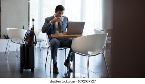 Businessman sitting airport terminal cafe using laptop and drinking coffee. Male entrepreneur  waiting for his flight. - Powered by Shutterstock