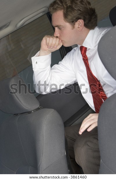 Businessman sitting in the\
back of the car contemplating while he wears a red tie and a white\
business shirt