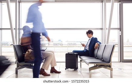 Businessman Sitting In Busy Airport Departure Lounge Using Mobile Phone - Shutterstock ID 1572235315