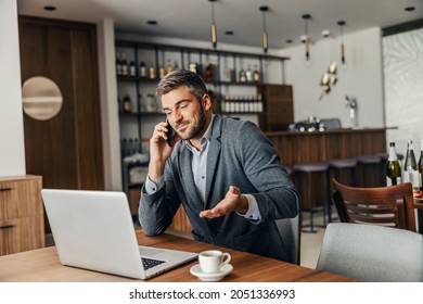 A businessman is sitting in the cafeteria and solving problems over the phone. There is a laptop on a table. A businessman and his remote business - Shutterstock ID 2051336993