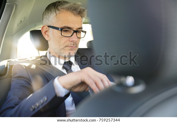 Businessman sitting in car backseat working on\
digital tablet