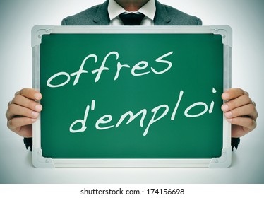 businessman sitting in a desk holding a chalkboard with the text offres d'emploi, jobs in french, written in it