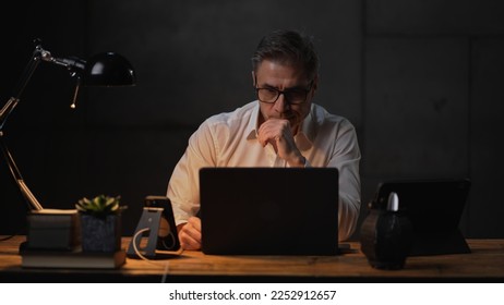 Businessman sitting at desk with laptop computer. Entrepreneur working late in office. Older, middle aged, mid adult, man in his 40s or 50s in business casual. - Powered by Shutterstock