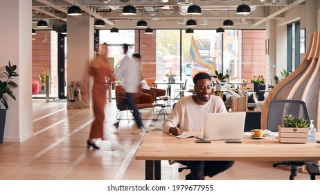 Businessman Sitting At Desk Writing In Notebook In Modern Open Plan Office