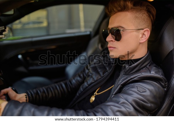 A businessman is sitting in a golden car. A man is\
driving inside a car. Driver. Chic man with glasses, with a perfect\
haircut, glasses, fashionable. Freelancer. Rich boy. A teenager\
drives a car.