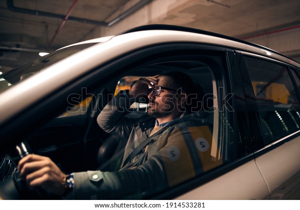 Businessman sitting in his\
car stuck in traffic. He is holding his hand on a forehead and\
nervously waiting