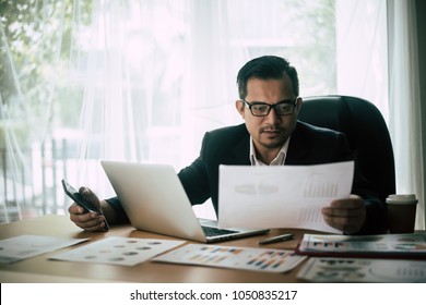 Businessman sitting at his workplace in front of laptop computer while doing some business paperwork. - Shutterstock ID 1050835217
