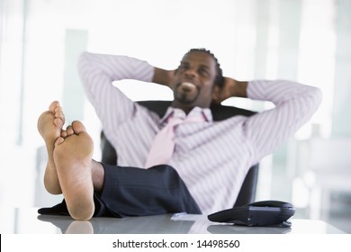 Businessman sitting in office with feet on desk relaxing and smiling
