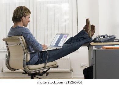 Businessman Sitting In Office With Feet Up On Desk, Using Laptop In Lap, Profile