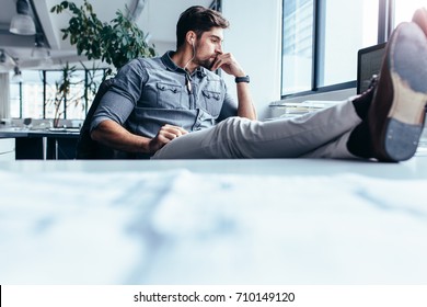Businessman sitting in office and listening music. Thoughtful man sitting with feet on table in office.