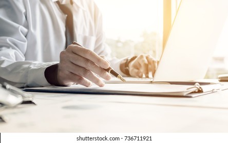 Businessman sitting at office room holding pen pointing summary report graph and using laptop for searching information data.