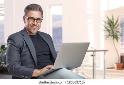 Businessman sitting in office working with laptop computer. Business portrait of older man.