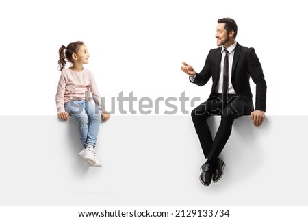 Businessman sitting on a blank panel and talking to a little girl isolated on white background