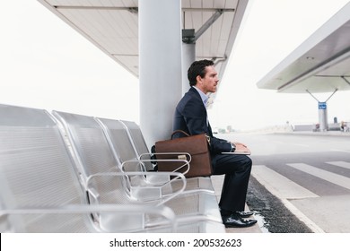 Businessman sitting on the chair at the airport bus stop and looking away, side view