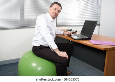 Businessman Sitting On Exercise Ball At Desk