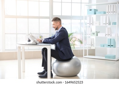 Businessman Sitting On Fitness Ball While Working In Office