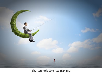 Businessman sitting on green moon and fishing with rod