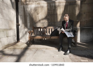 Businessman Sitting On Outdoor Bench Reading Newspaper