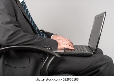Businessman sitting and typing on his laptop, on grey background