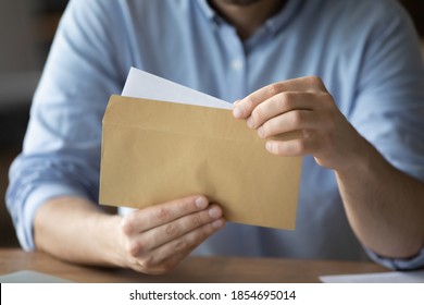 Businessman sitting at workplace desk holding yellow envelope take out received paper letter notice sheet, close up image. Business correspondence, corporate news, notification or invitation concept