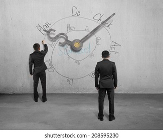 Businessman sketching PDCA cycle on concrete wall with clock hands