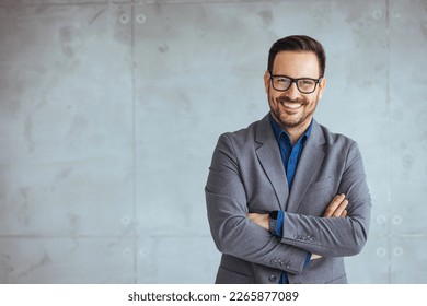 Businessman smiling with arms crossed on white background. Portrait of young happy businessman wearing grey suit and blue shirt standing in his office and smiling with arms crossed
