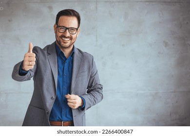 Businessman smiling with arms crossed on white background. Portrait of young happy businessman wearing grey suit and blue shirt standing in his office and smiling. Businessman giving thumbs up - Shutterstock ID 2266400847
