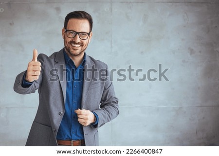 Businessman smiling with arms crossed on white background. Portrait of young happy businessman wearing grey suit and blue shirt standing in his office and smiling. Businessman giving thumbs up