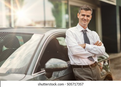 Businessman Smiling At Camera And Leaning Against His New Expensive Car, Dealership And Business Concept