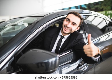 Businessman smiling at camera showing thumbs up in his car