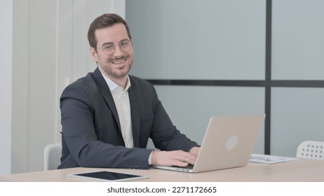 Businessman Smiling at Camera while using Laptop