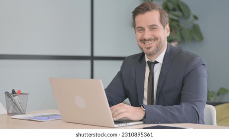 Businessman Smiling at Camera while Working on Laptop