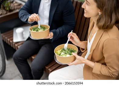 Businessman and smiling caucasian businesswoman eating salad while having lunch at work. Concept of healthy eating. Idea of rest and break on job. Business people sitting on bench outdoors - Powered by Shutterstock