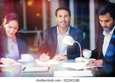 Geschäftsmann lächelt, während Kollegen im Büro auf Papier schreiben