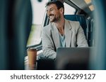 Businessman smiling while commuting on a train, working remotely on his laptop with a coffee, enjoying the journey