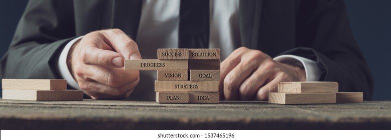 Businessman stacking wooden pegs with words of business strategy, vision and development on them in a conceptual image.  - Shutterstock ID 1537465196